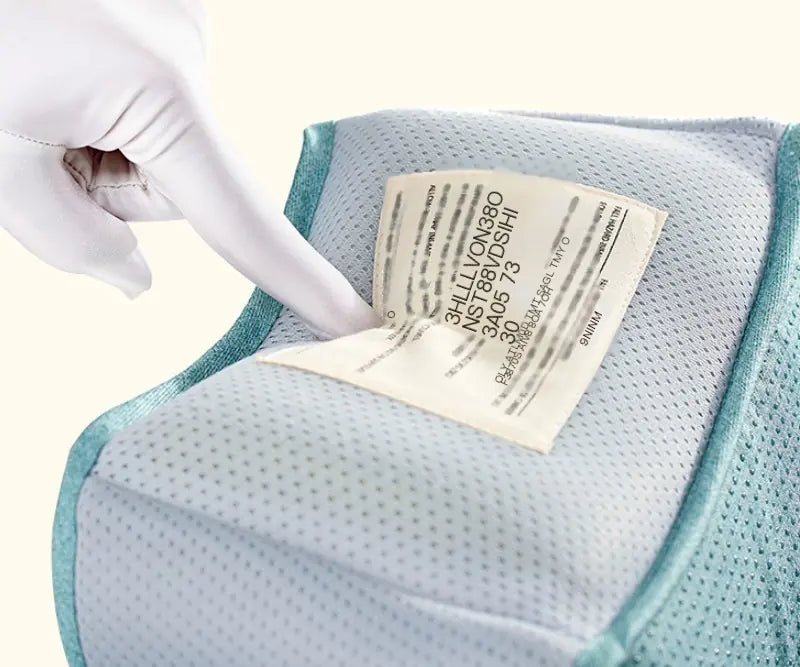 Fehér kesztyűs kéz érinti a címkét a csípőüléses medve hordozó belsejében, elől hordozáshoz.